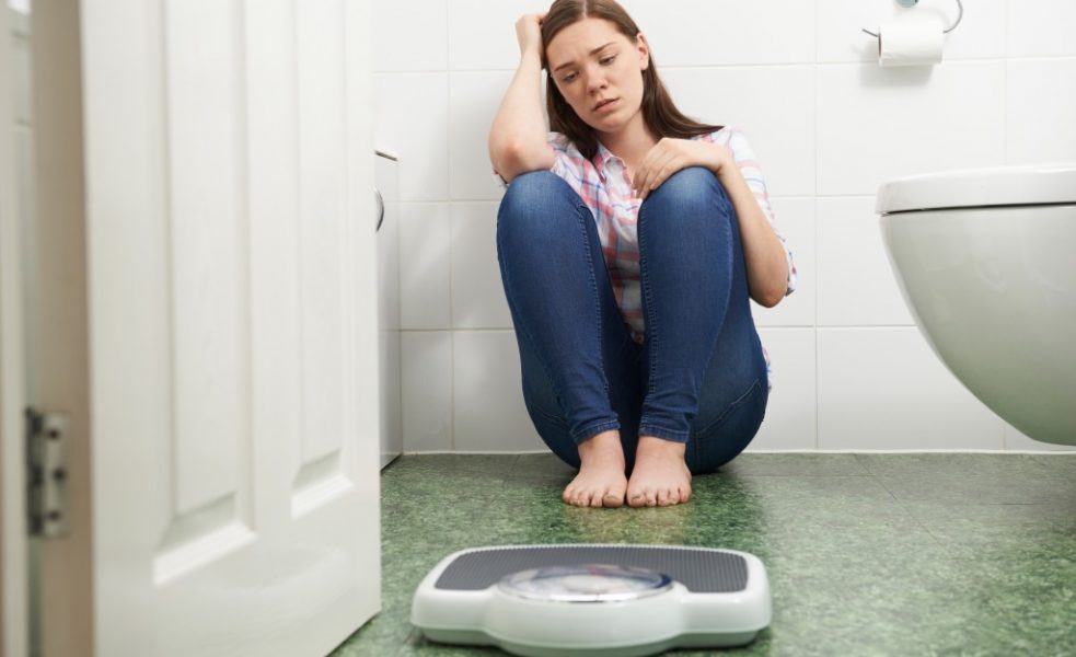 Young girl sitting on the floor next to weighing scale