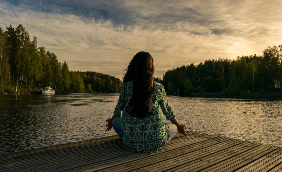 woman meditating near a lake